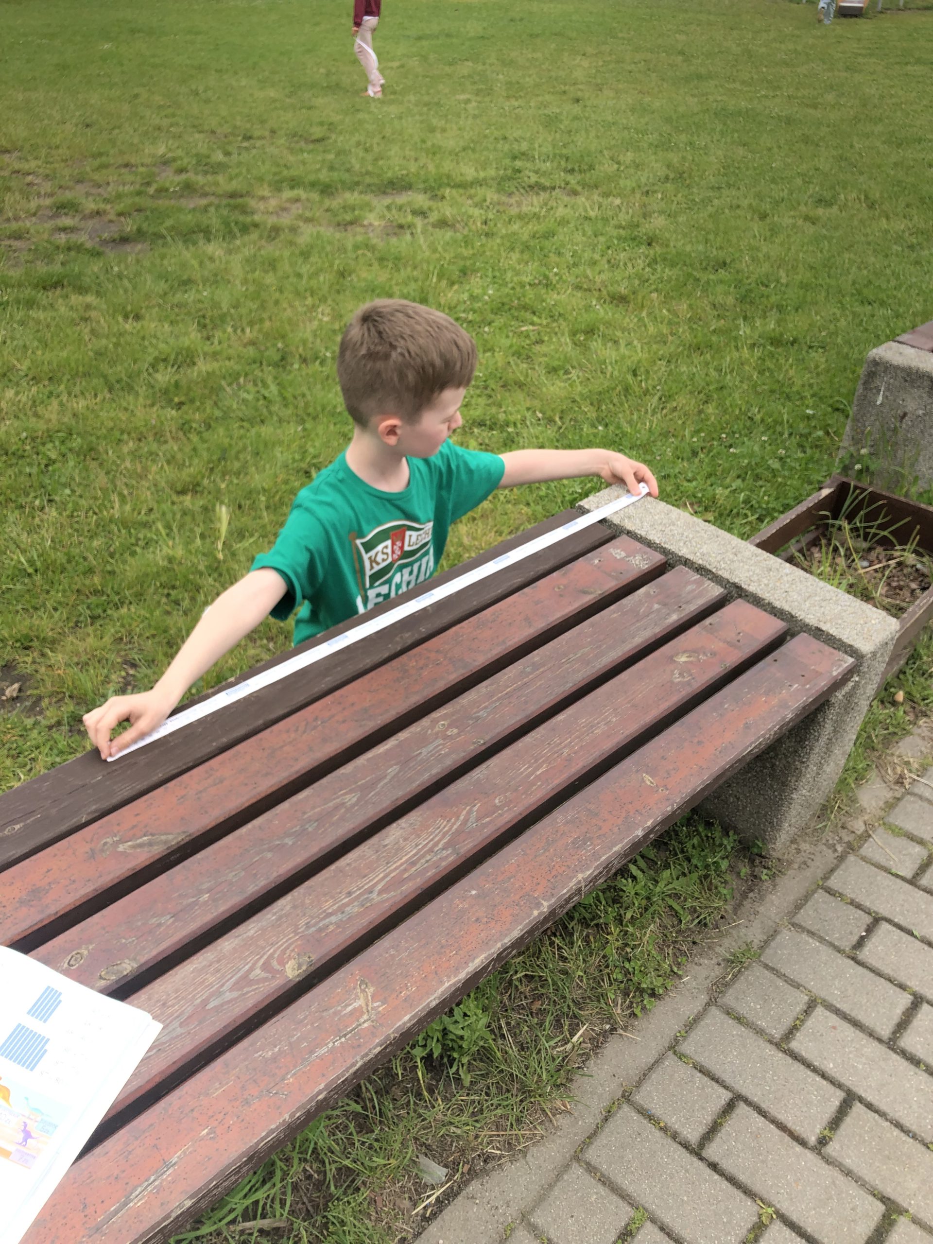 chłopiec kucając mierzy centymetrem ławkę.