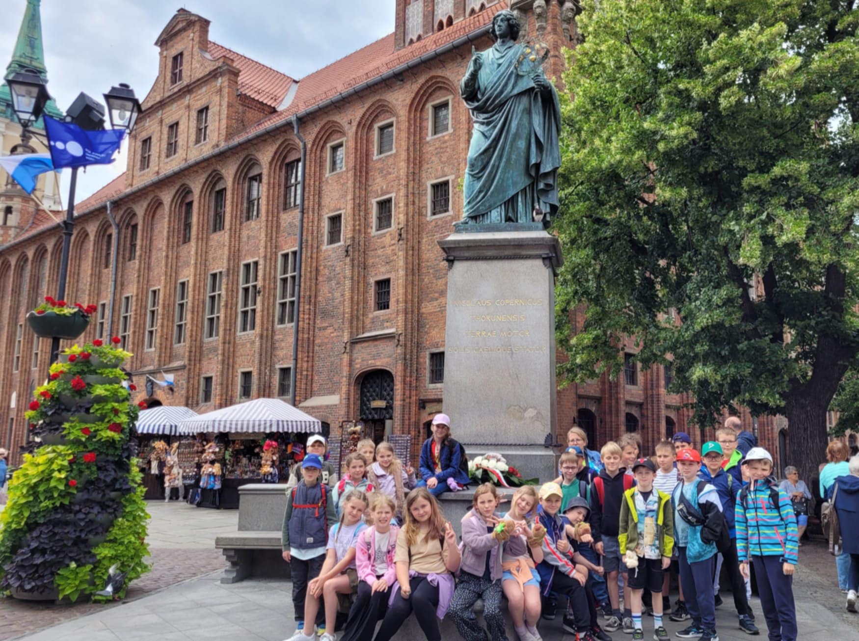 Uczniowie klasy 3a stoją z nauczycielką pod pomnikiem Mikołaja Kopernika w Toruniu.
