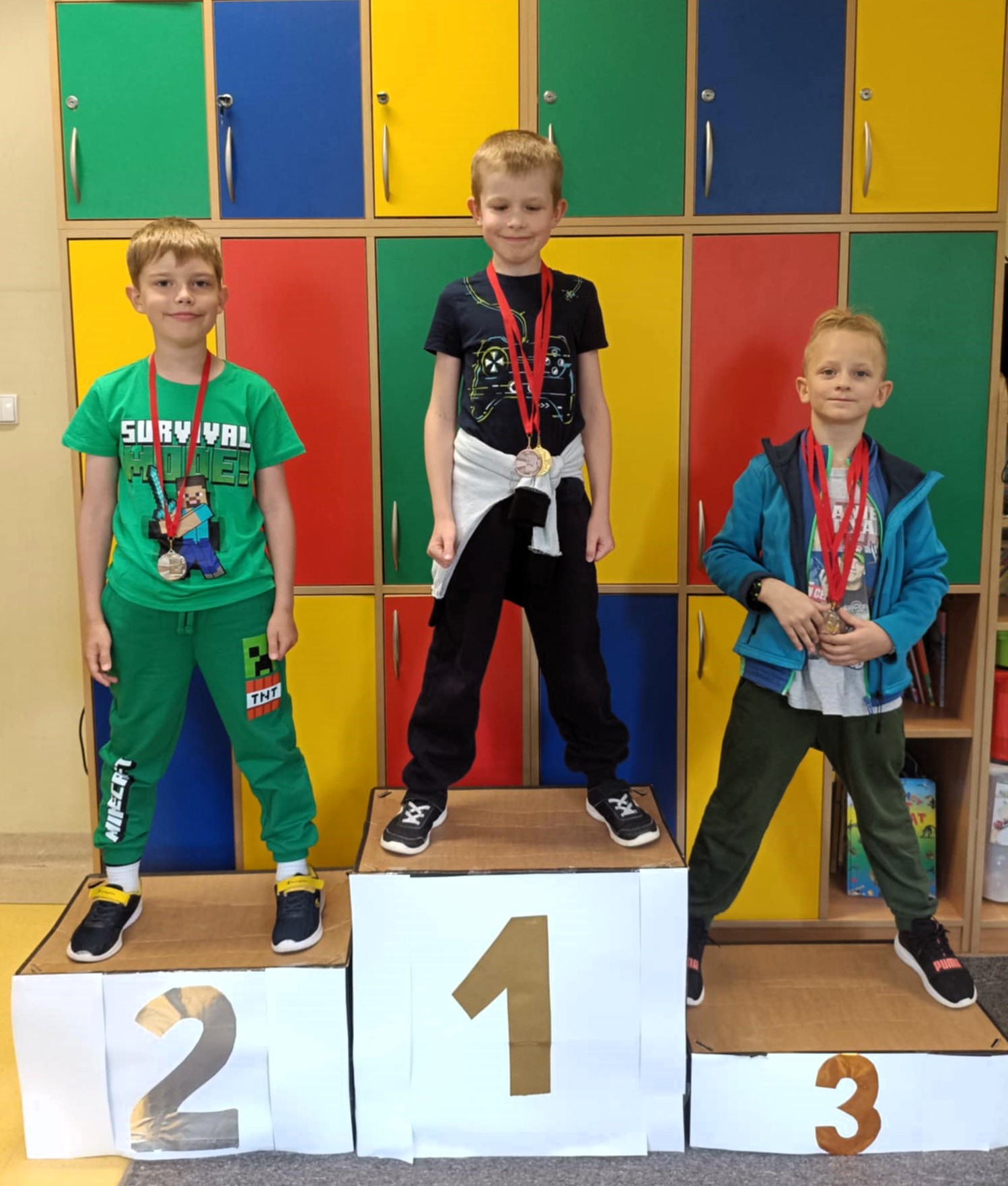 3 chłopców stoi na podium. Na szyi mają zawieszone medale.