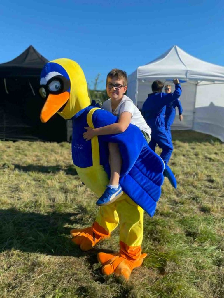 Chłopiec/uczeń  siedzi na plecach Osoby która jest przebrana na ptaka - maskotkę lotniska