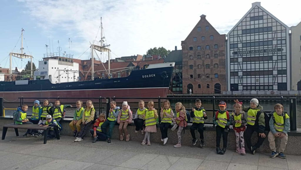 Na tle statku Sołdek oraz budynku Muzeum Morskiego nad Motławą pozują do zdjęcia uczniowie klasy 1c.