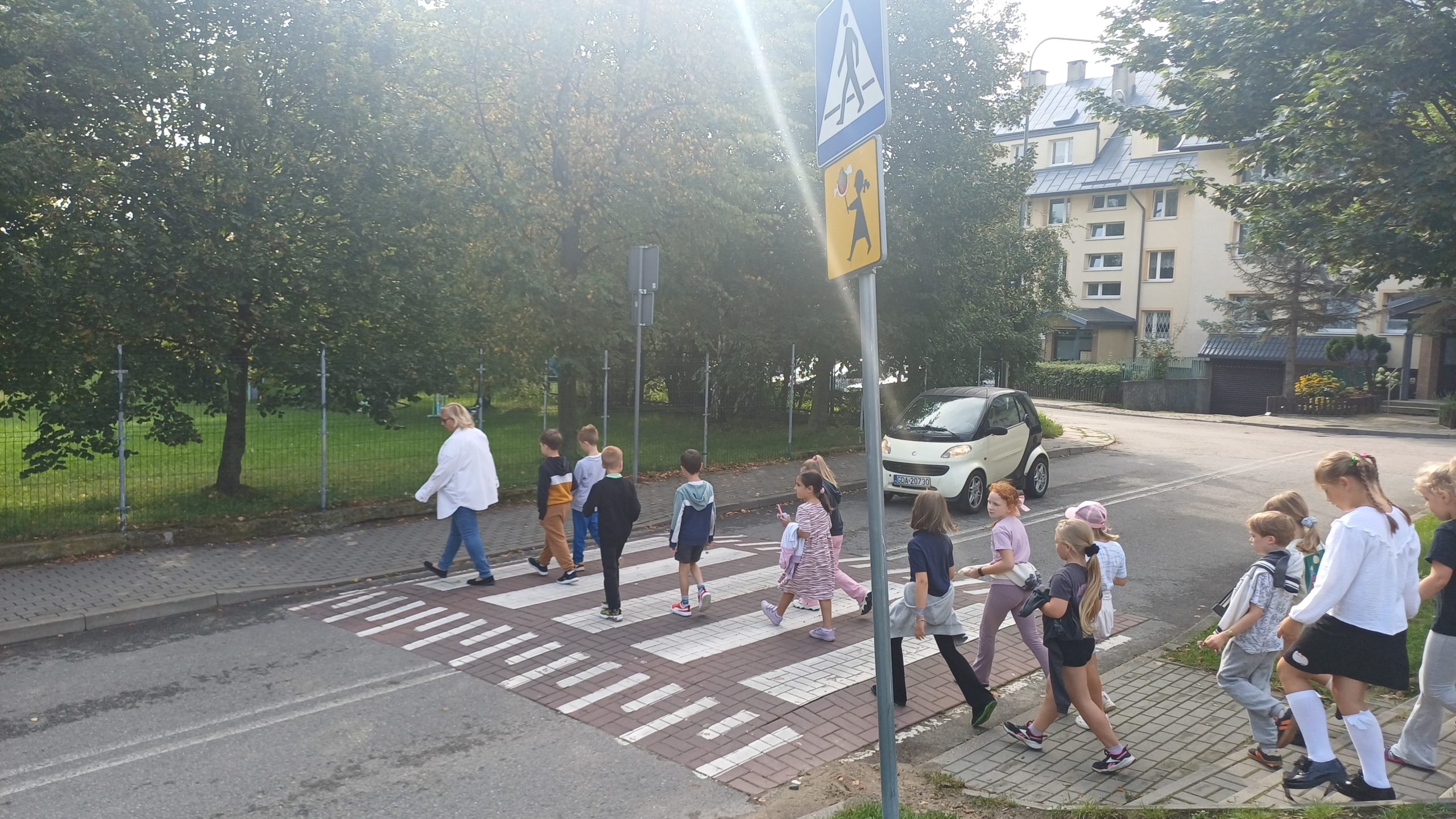 Nauczyciel z grupą 14 dzieci przechodzi przez przejście dla pieszych.