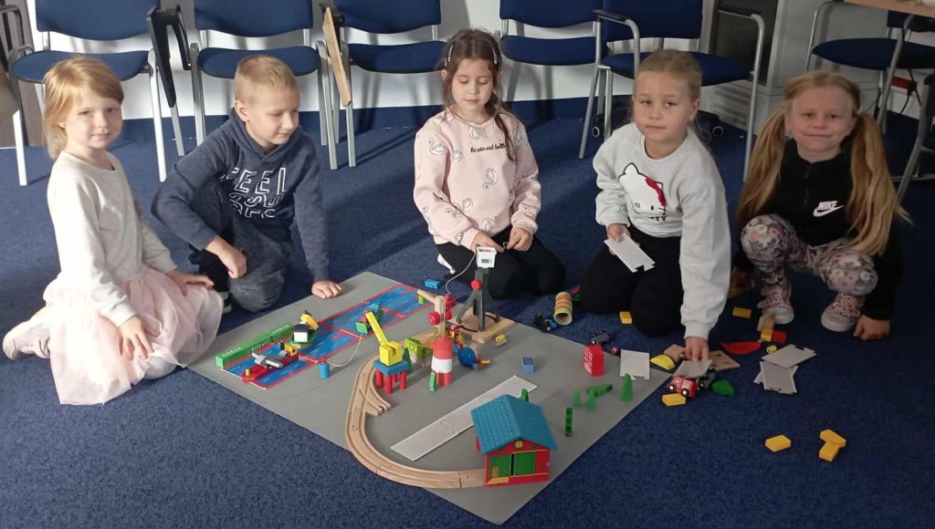 Pięcioosobowa grupa uczniów klasy 1c przed swoją makietą portu zbudowaną z drewnianych klocków.