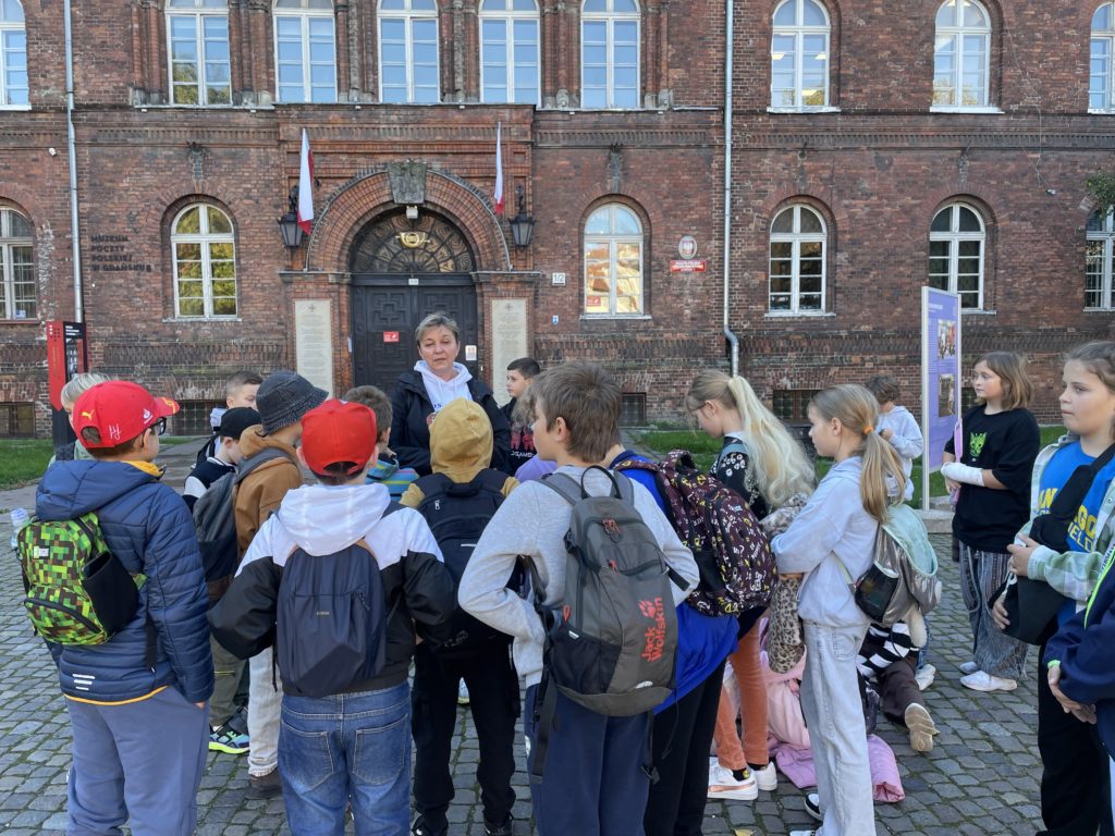 Grupa uczniów słucha Pani przewodnik przed wejściem do budynku Poczty Polskiej w Gdańsku.