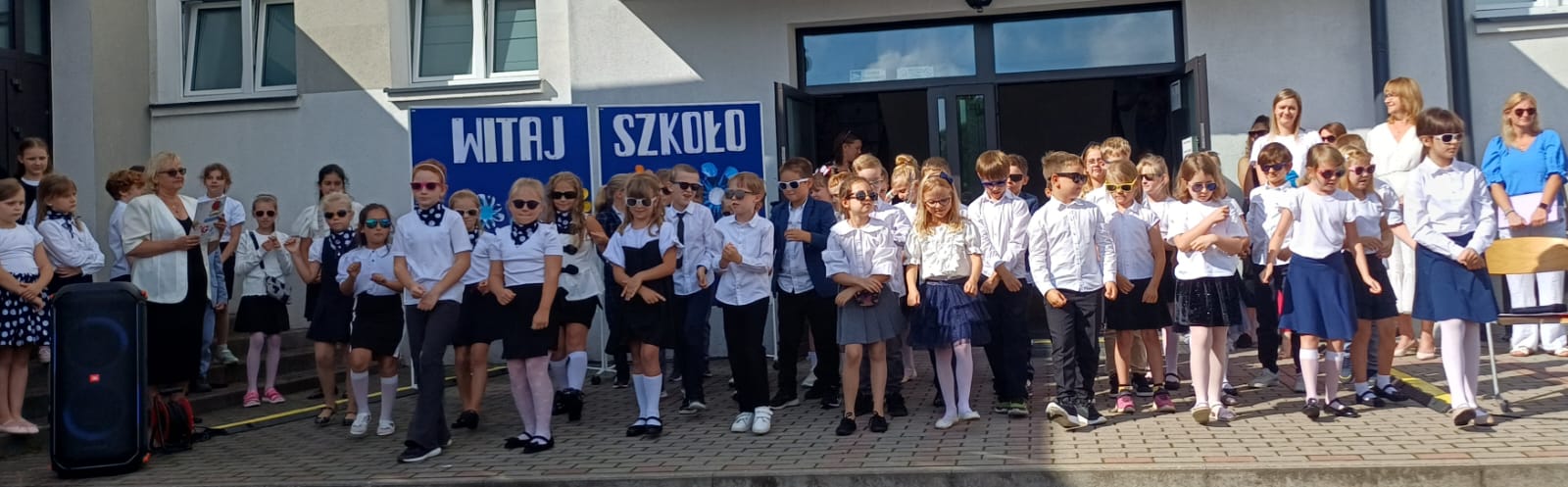 Grupa dzieci tańczy przed wejściem do szkoły.