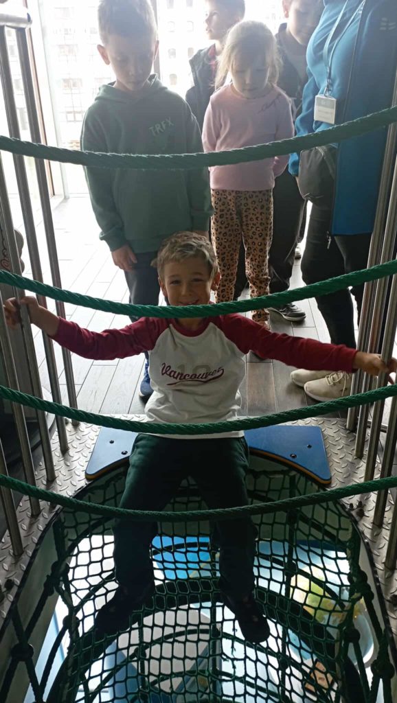 Na pierwszym planie siedzący chłopiec, czekający na wejście do rękawa ewakuacyjnego. Przed rękawem inni uczniowie klasy 1c.