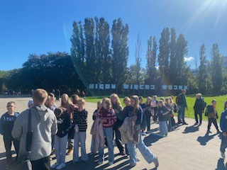 Grupa młodzieży stoi przy napisie „Nigdy więcej wojny” w słoneczny dzień, podczas wycieczki edukacyjnej