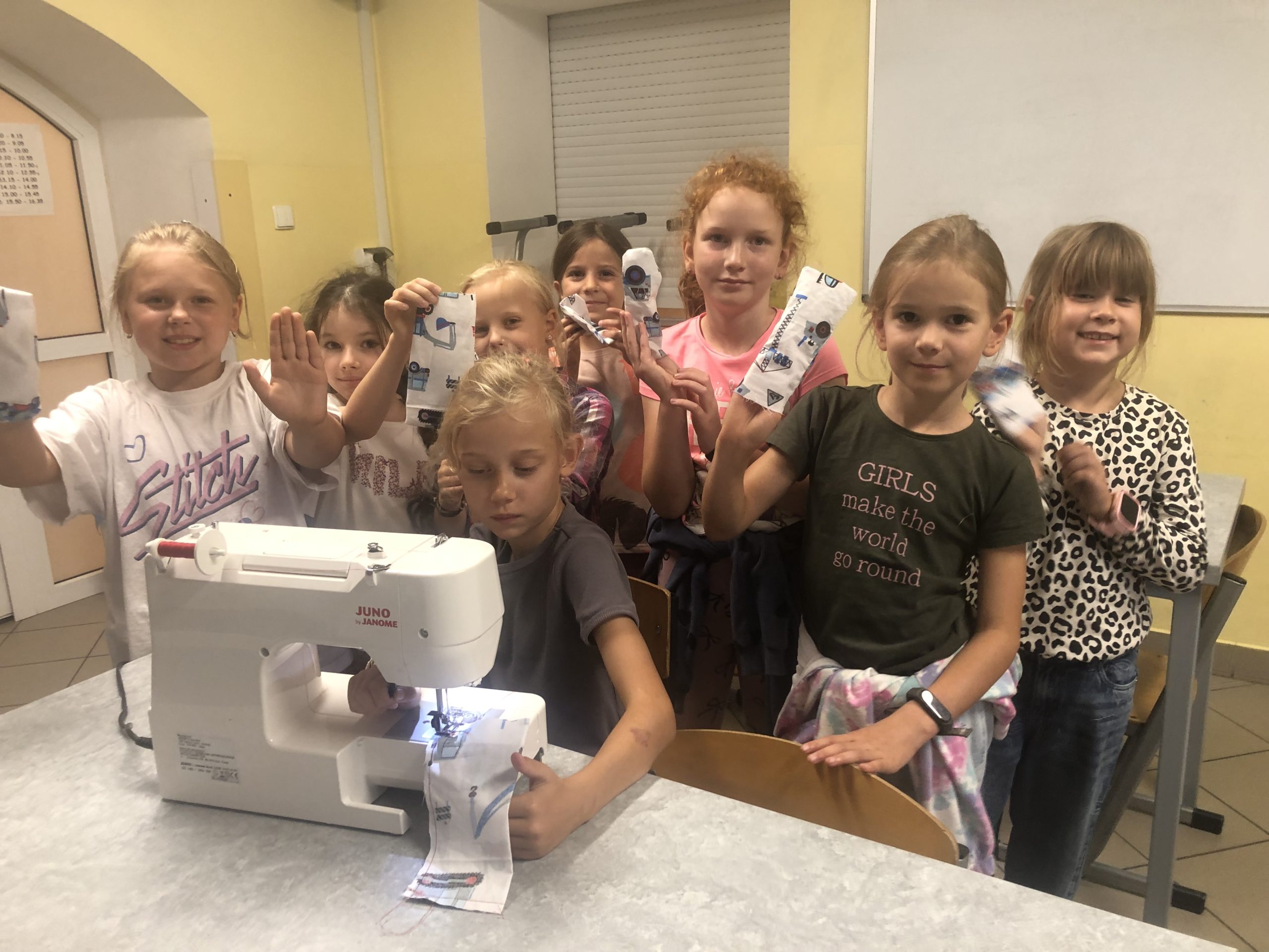 7 dziewczynek stoi za uczennicą siedzącą przy maszynie do szycia.