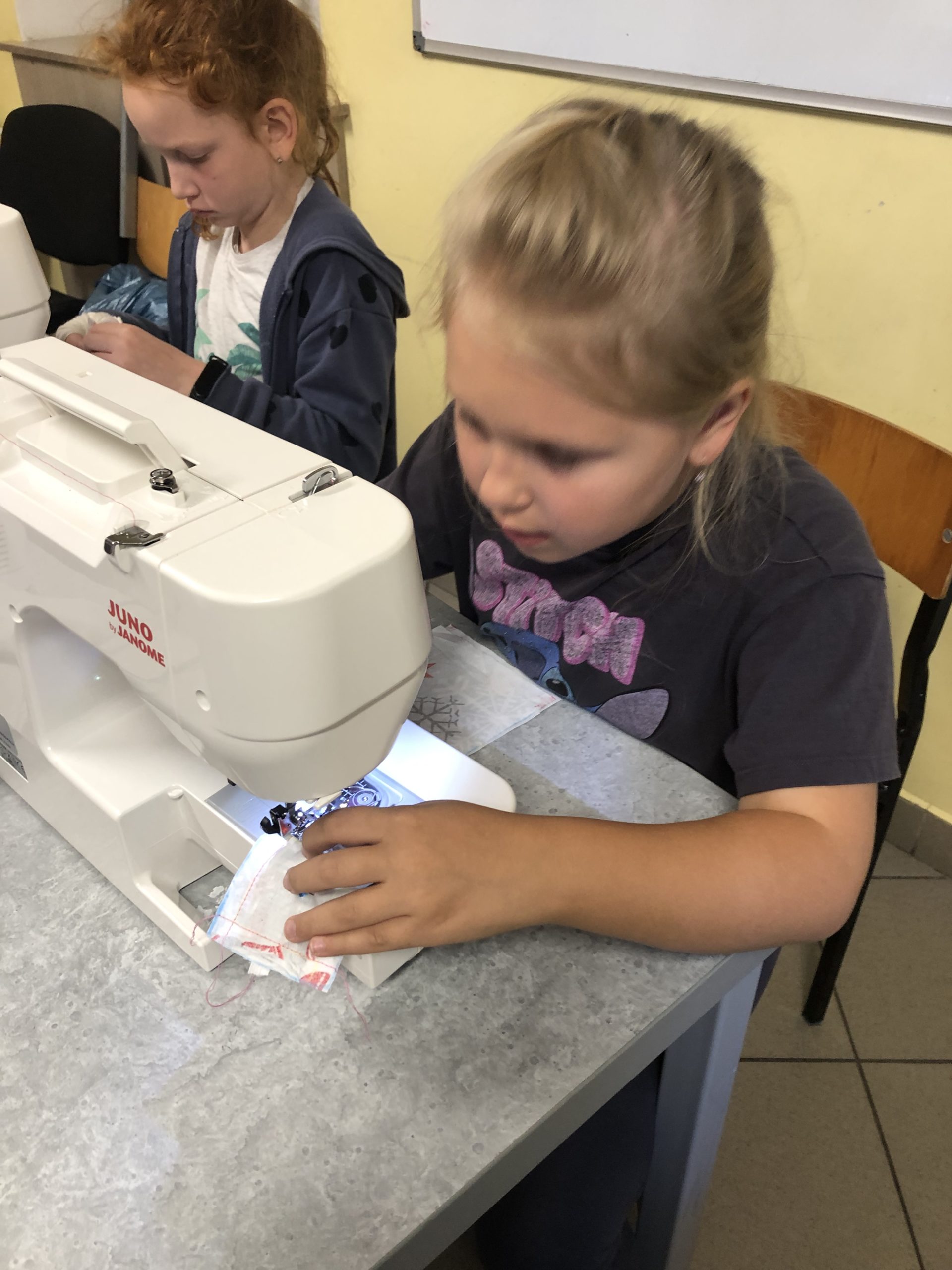 Dwie dziewczynki siedzą przy maszynach do szycia.