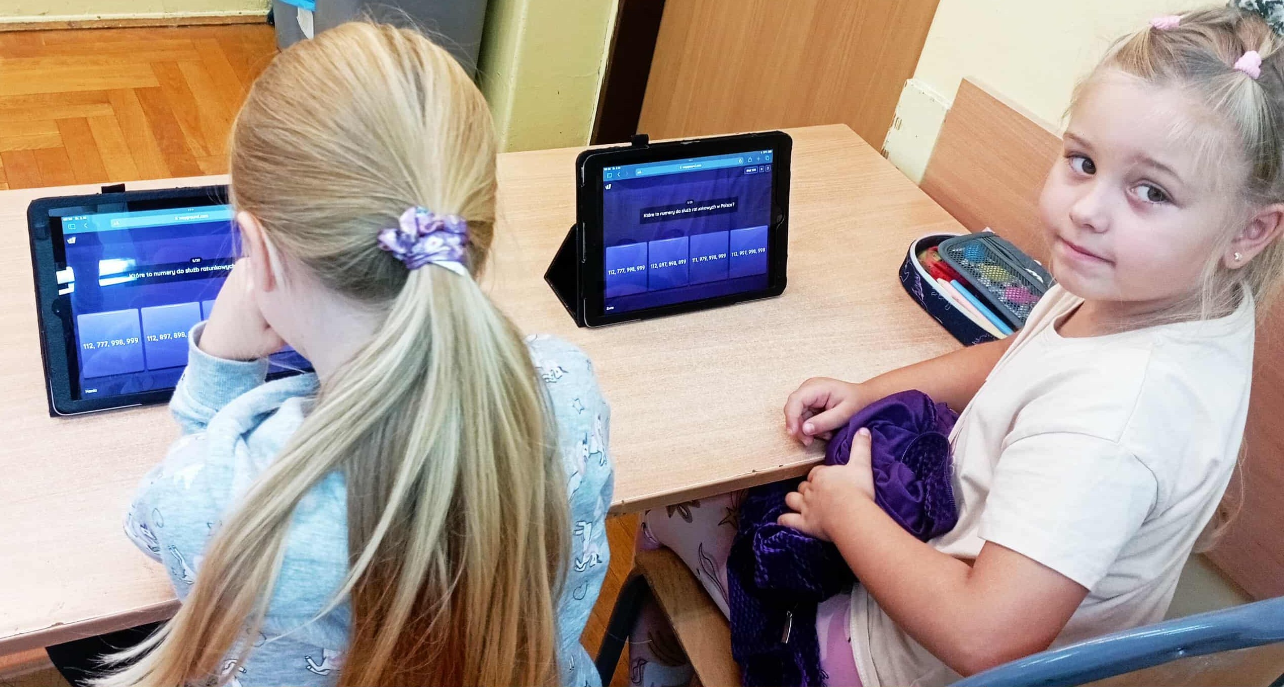 W sali lekcyjnej w ławce siedzą dwie uczennice klasy 1c. Przed nimi na ławce stoją IPady wyświetlające pytania z Quizizz.