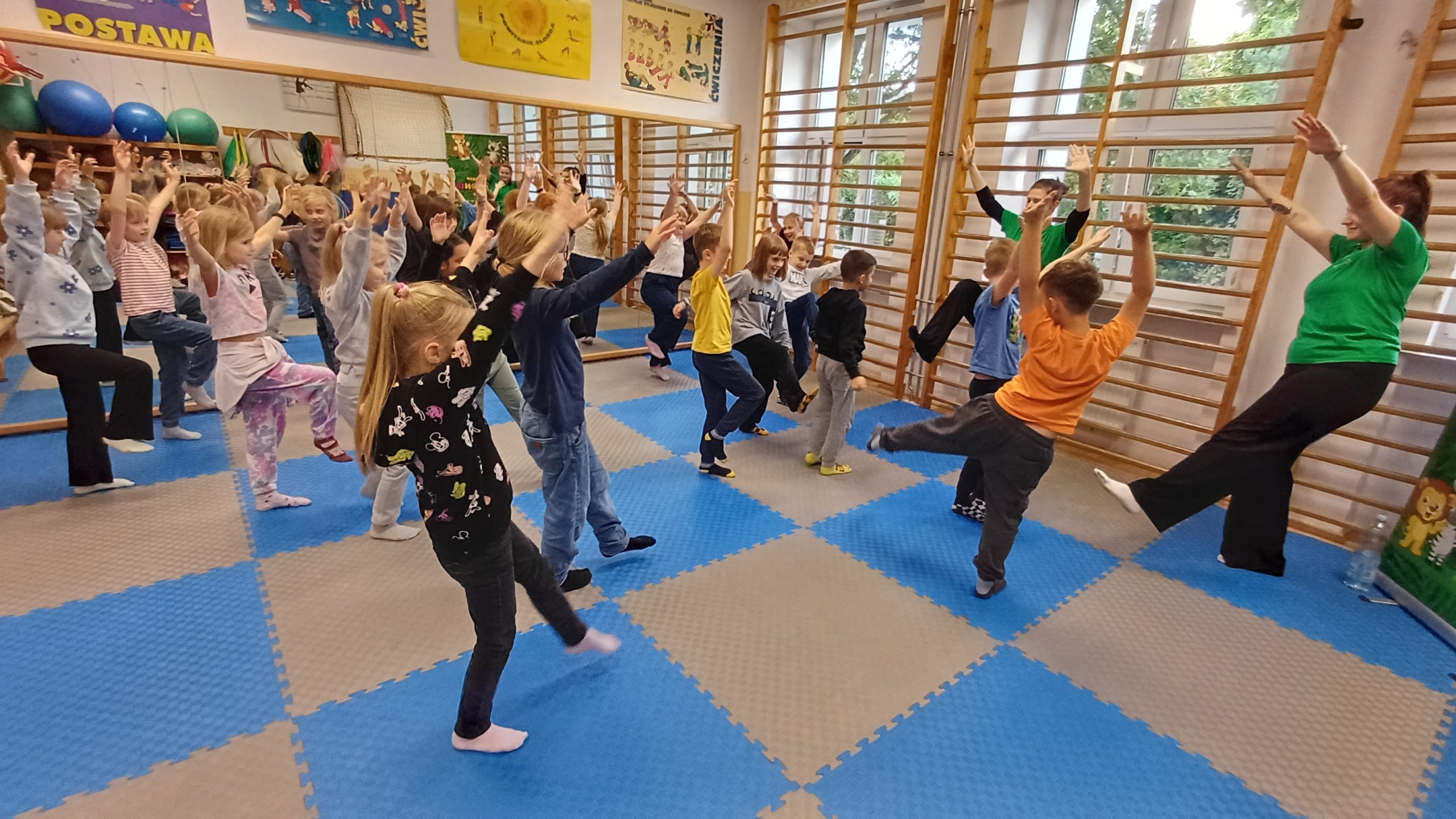 grupa dzieci i 2 panie stoją na jednej nodze w sali korekcyjnej 