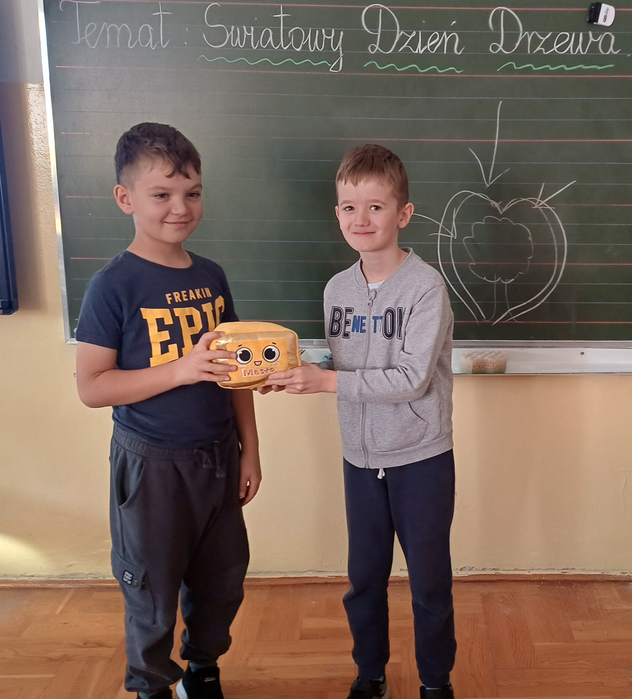 2chlopcow stoi pod tablicą, skierowanych sa do siebie twarzami, uśmiechają się do siebie