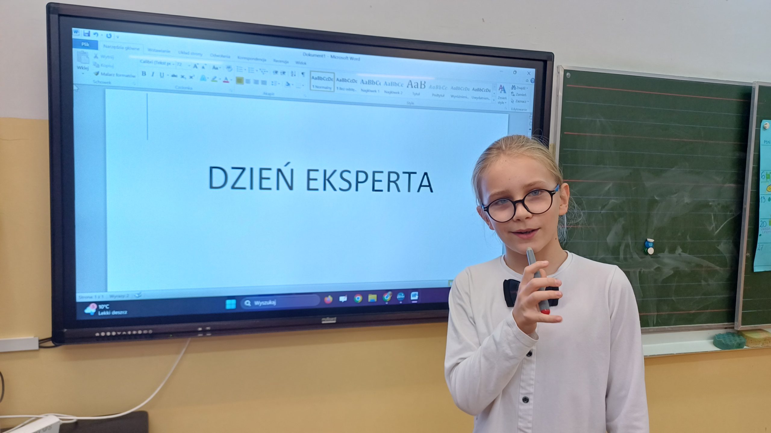 Chłopiec stoi przed tablicą, trzymając w ręku wskaźnik.