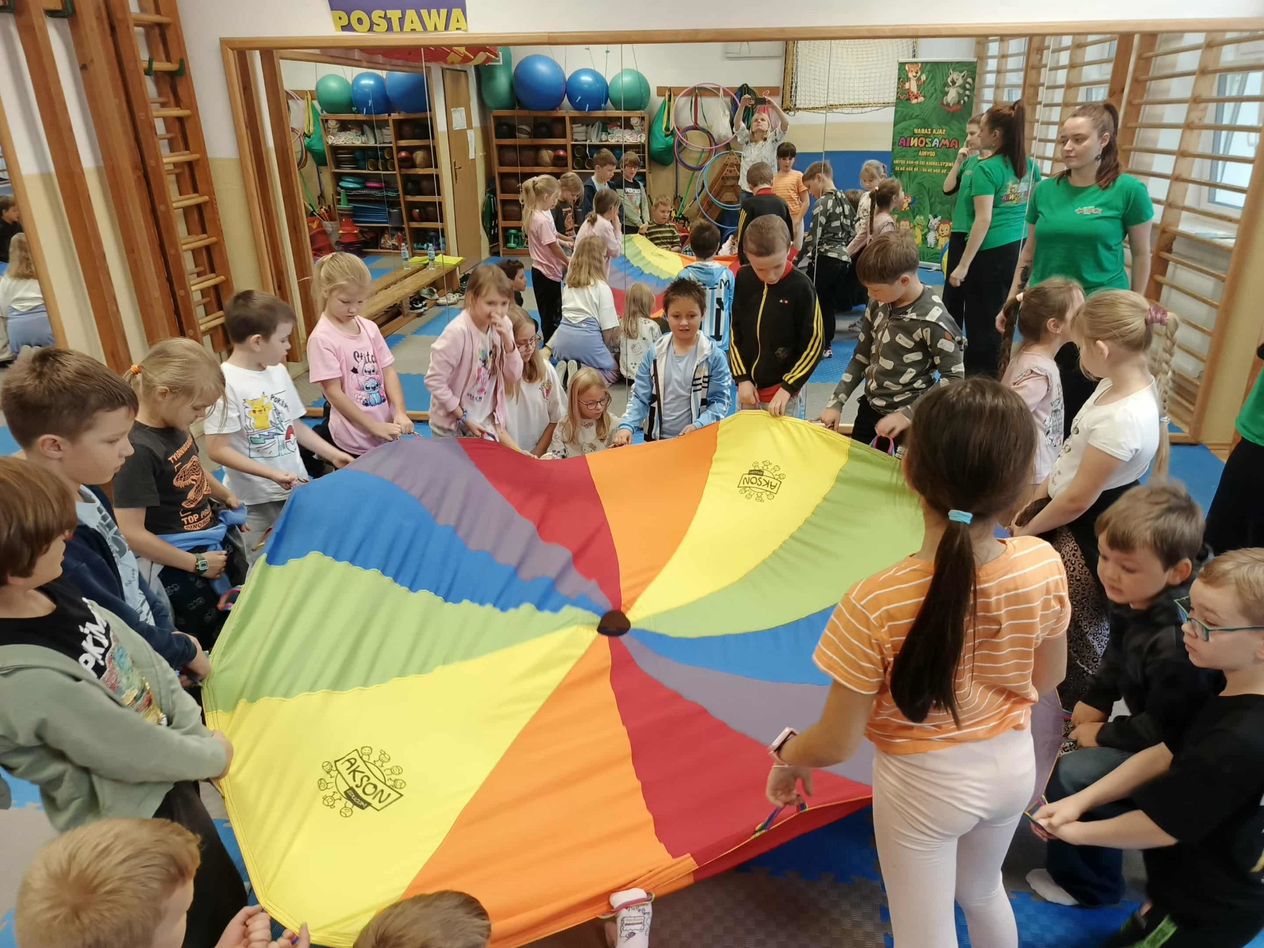  Grupa dzieci stoi w kole, trzymając chustę animacyjną