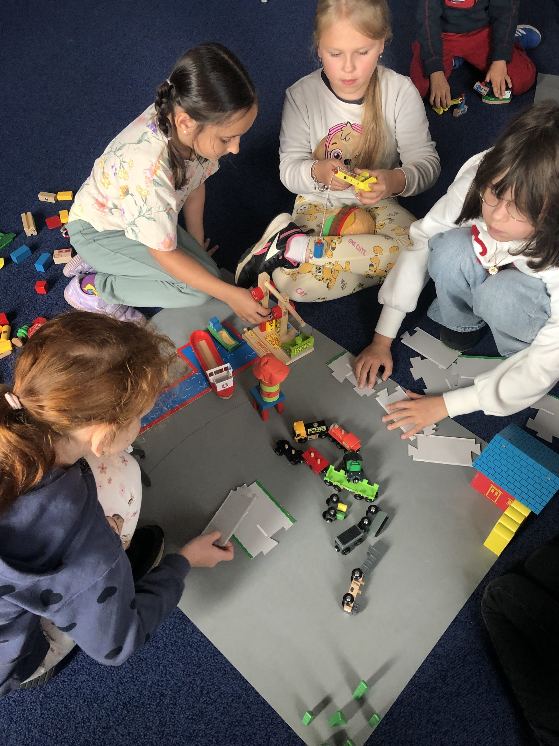  Cztery dziewczynki siedzą na dywanie skupione na budowaniu z klocków.