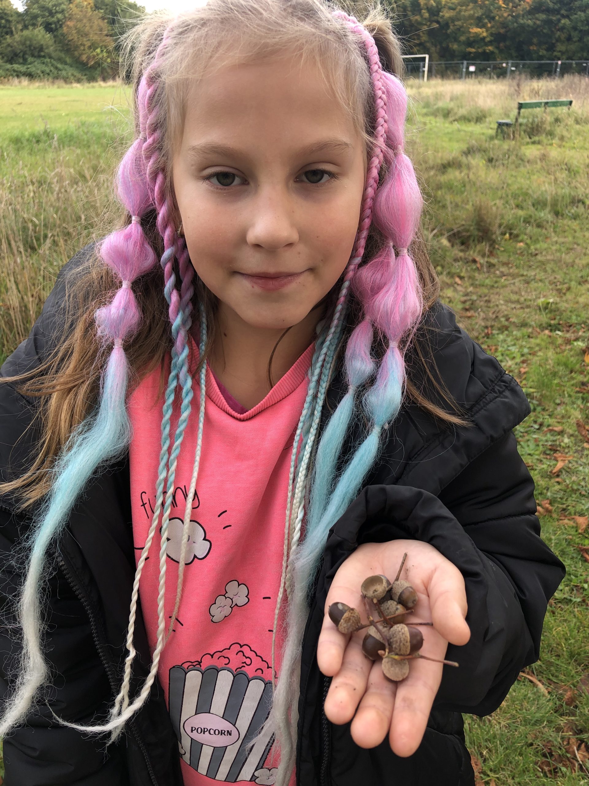 Dziewczynka na wyciągniętej dłoni prezentuje żołędzie.