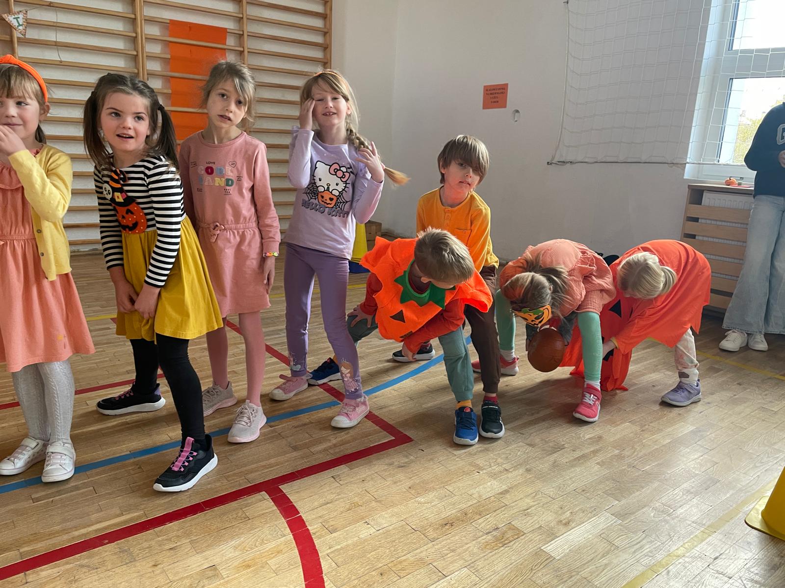 8 dzieci stoi w rzędzie podając sobie dynie pomiędzy nogami.