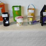 Blat nakryty białym obrusem, a na nim 10 lampionów. Niektóre z nich są podświetlone. Wszystkie mają przyczepioną małą karteczkę z imieniem, nazwiskiem i klasą.