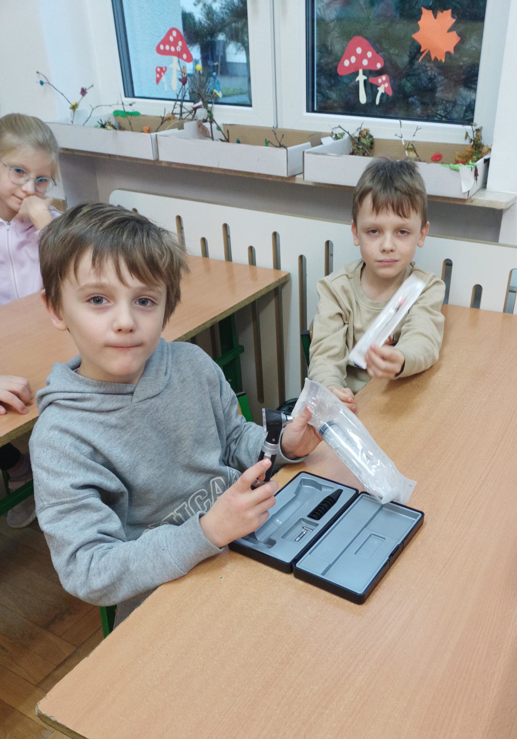 .378 Dwóch chłopców siedzących w ławce trzyma w dłoniach sprzęt przydatny w pracy weterynarza: otoskop i strzykawki.