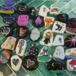 30 kamieni leży na wzorzystej podkładce. Kamienie są ozdobione kolorowymi rysunkami.