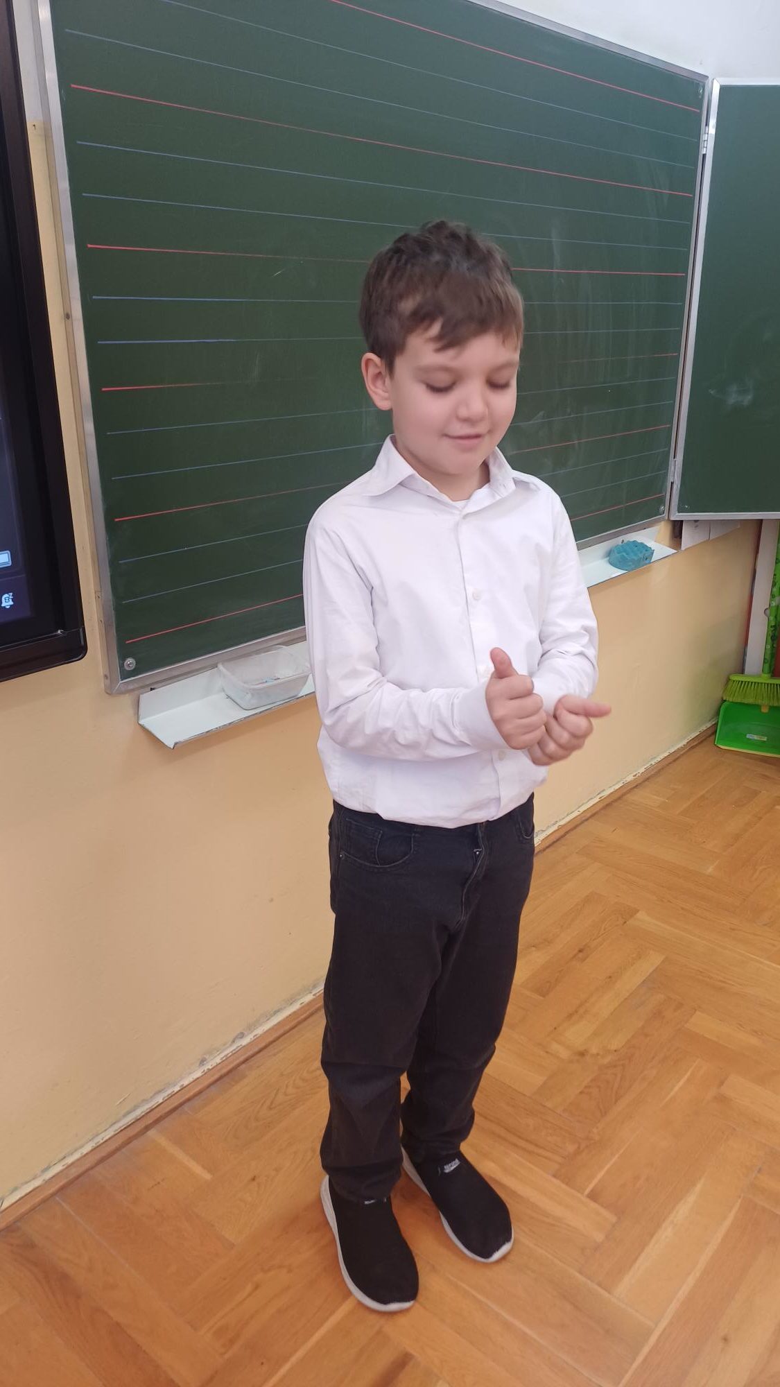  chłopiec ubrany na galowo stoi przed tablicą uśmiechając się