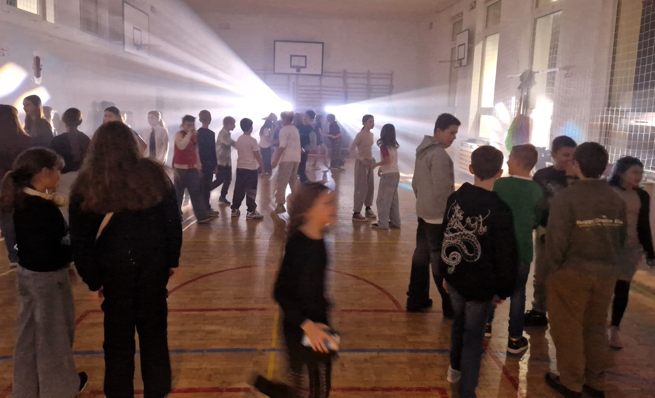 Grupa uczniów bawiących się na andrzejkowej dyskotece w sali gimnastycznej, w tle jasne światła i efekty sceniczne