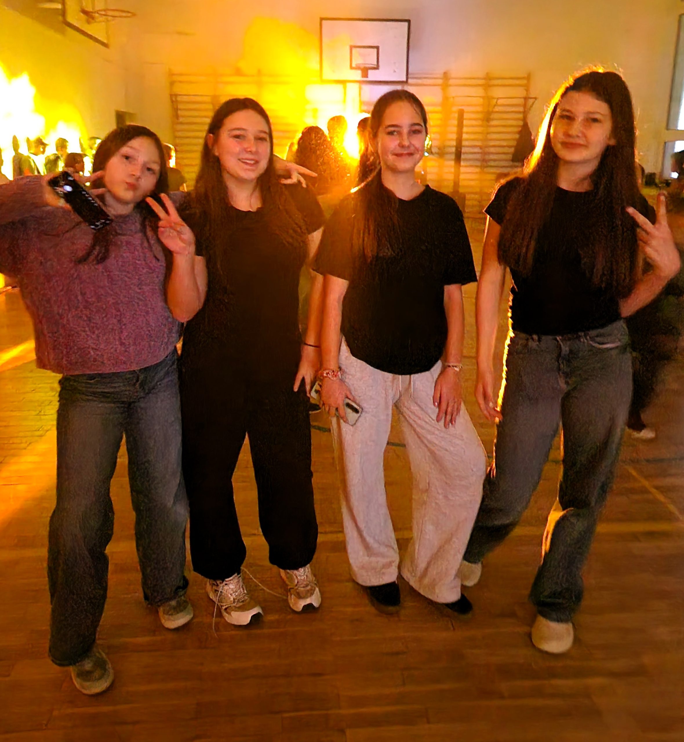 Cztery uczennice stojące razem na sali gimnastycznej podczas dyskoteki andrzejkowej, pozujące do zdjęcia w kolorowym świetle.