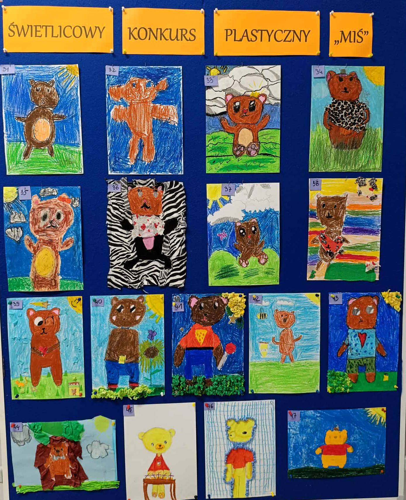 Zdjęcie przedstawia tablicę ekspozycyjną z kolorowymi pracami plastycznymi dzieci, uczestników konkursu „Świetlicowy Konkurs Plastyczny – Miś”. Na ciemnoniebieskim tle przypiętych jest kilkanaście rysunków misiów wykonanych różnymi technikami. 