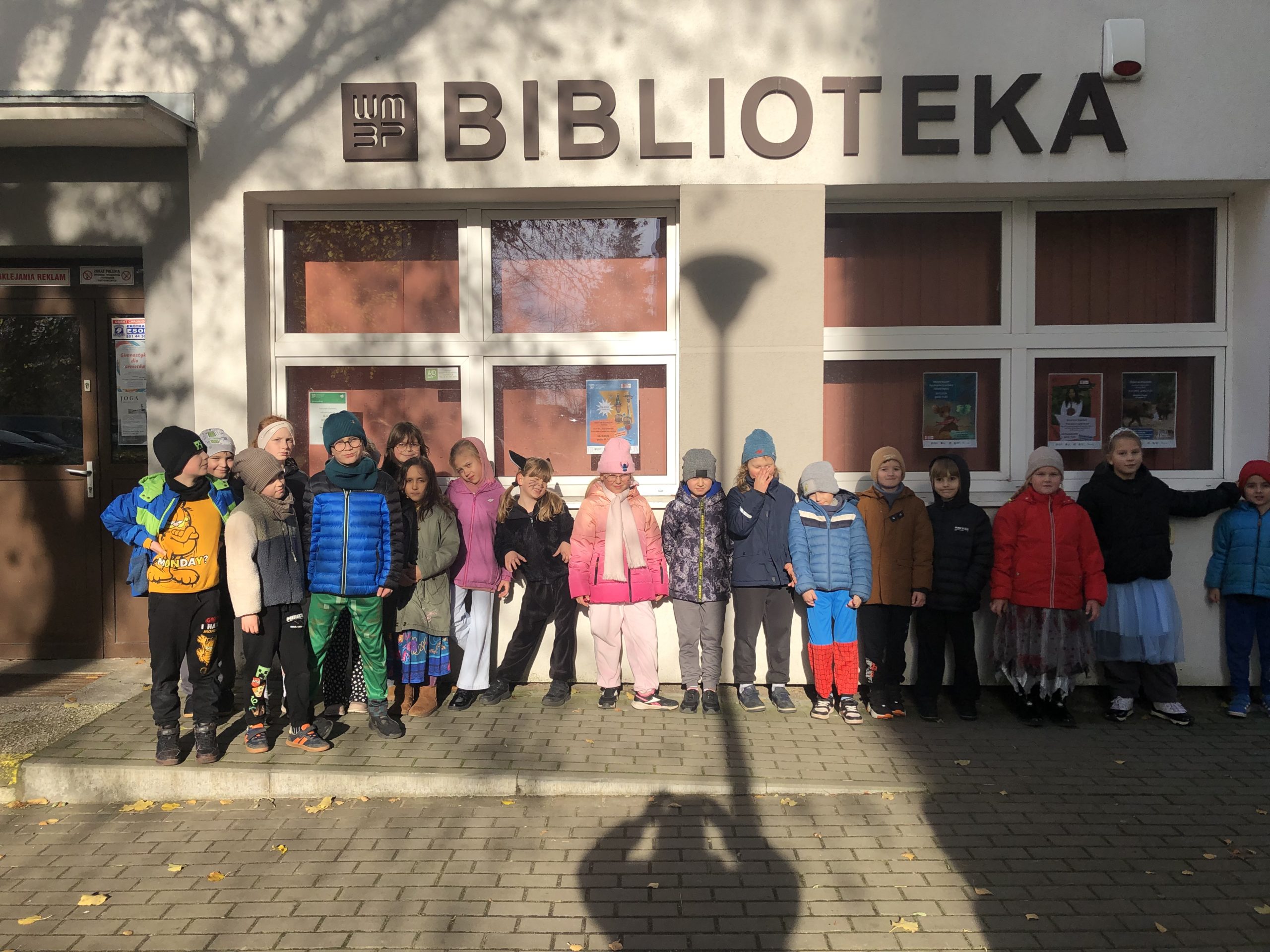 Grupa 19 uczniów stoi przed budynkiem biblioteki.