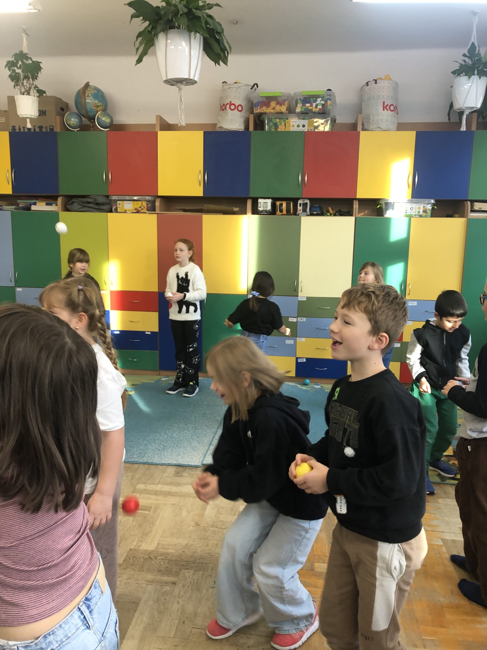  9 dzieci chodzi po sali podrzucając małe piłeczki. 