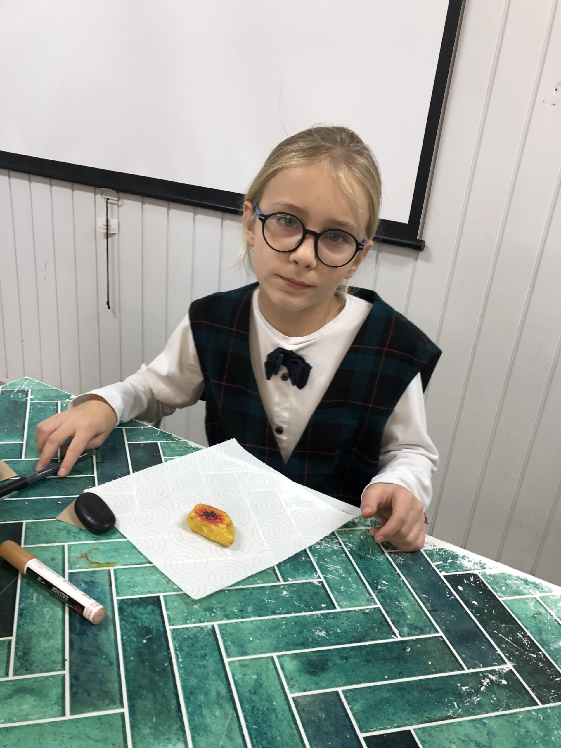 Uczeń siedzi przy stole na którym leży pomalowany kamień.