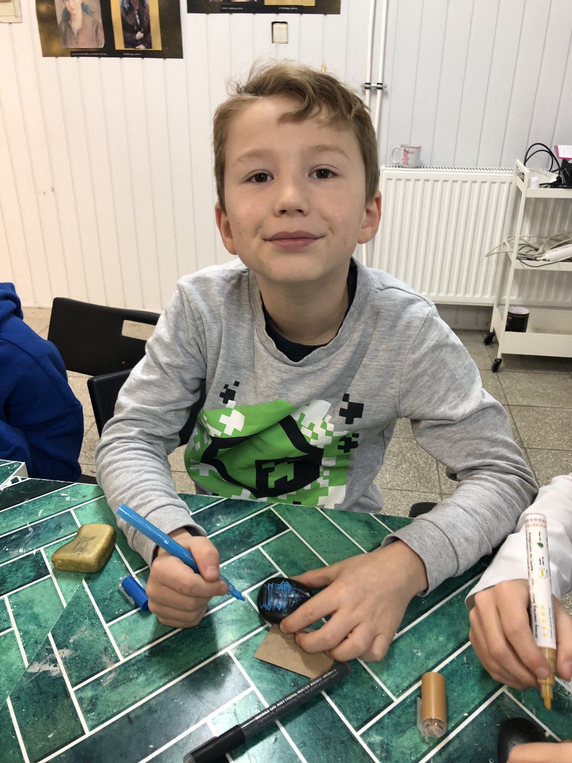 Chłopiec siedzi przy stole, w rękach trzyma mazak i kamień.