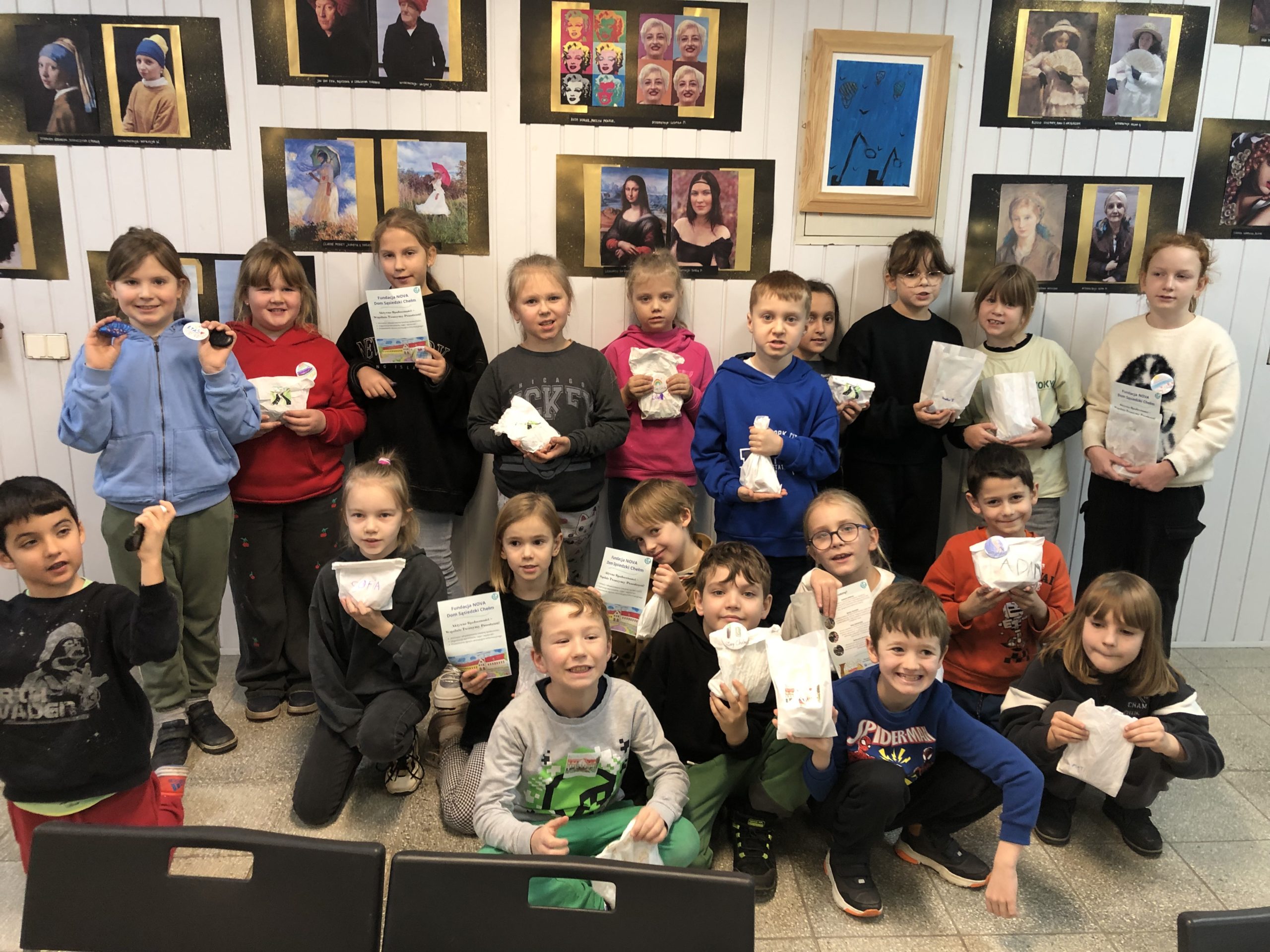 Grupa 11 dzieci siedzi przy stole i słucha pani stojącej z tylu stołu