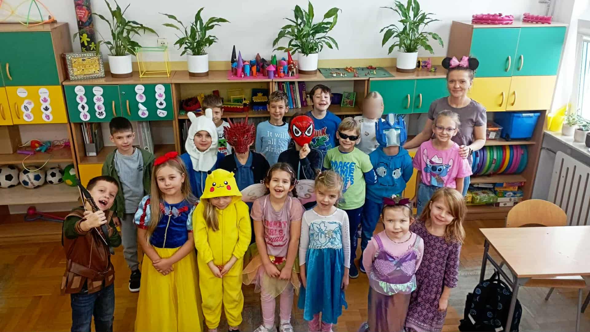 Uczniowie klasy 1c przebrani za postacie z bajek – m.in. królewny, wróżki, superbohaterowie i bajkowe zwierzątka – pozują wspólnie w sali podczas Dnia Postaci z Bajek.