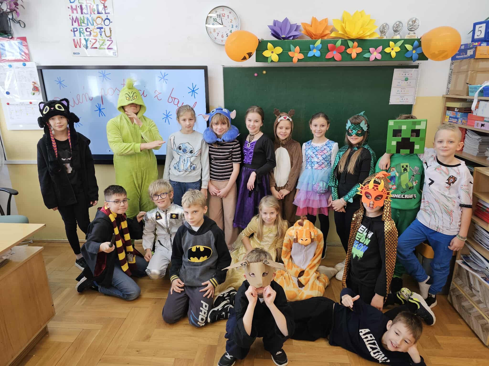 Uczniowie klasy 3a przebrani za postacie z bajek – m.in. królewny, wróżki, superbohaterowie i bajkowe zwierzątka – pozują wspólnie w sali za nimi widoczna tablica i ekran monitora.