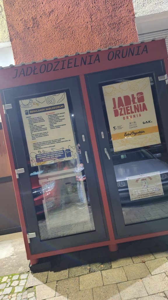 djęcie przedstawia Jadłodzielnię Orunia - lodówki, która jest zabudowana w specjalny sposób. Miejsce, z którego osoby potrzebujące mogą wziąć jedzenie, które ktoś wcześniej tam umieścił.