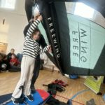 Uczennica trzyma w rękach żagiel, stoi na desce do pływania