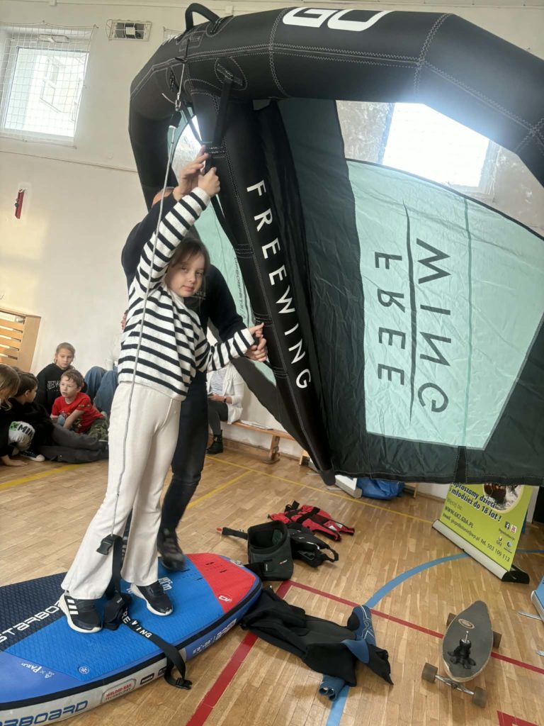 Uczennica trzyma w rękach żagiel, stoi na desce do pływania