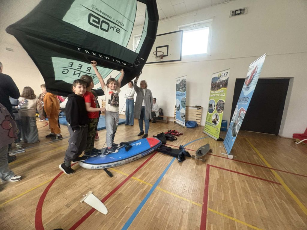 Grupa uczniów stoi na desce do pływania za nimi dmuchany żagiel