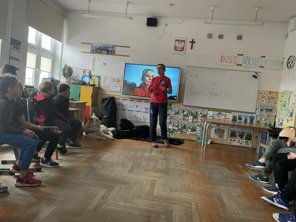 Opiekunka psów opowiada o ich pracy pokazując filmik uczniowie siedzą w półkolu