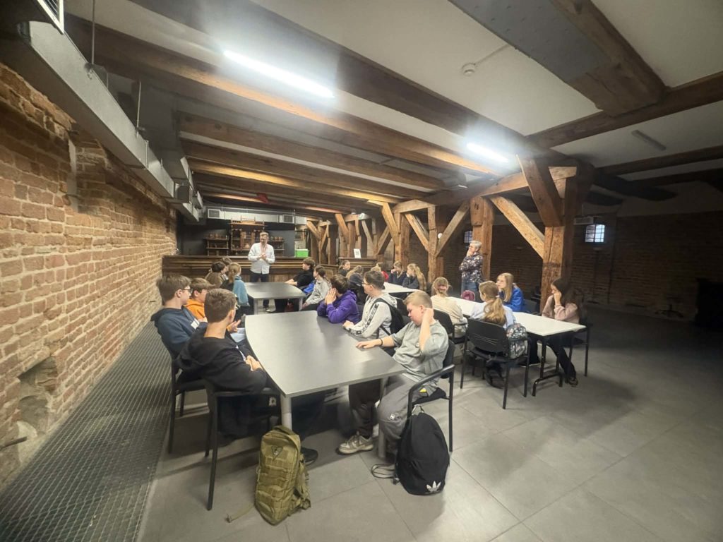 Grupa dzieci siedzi przy stołach w muzeum archeologicznym