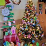 Szkolna dekoracja świąteczna w matematycznym stylu. Choinka i lampiony są ozdobione własnoręcznie wykonanymi ozdobami z figurami geometrycznymi, liczbami i symbolem π. Całość tworzy kolorową i pomysłową ekspozycję przygotowaną na szkolny konkurs.