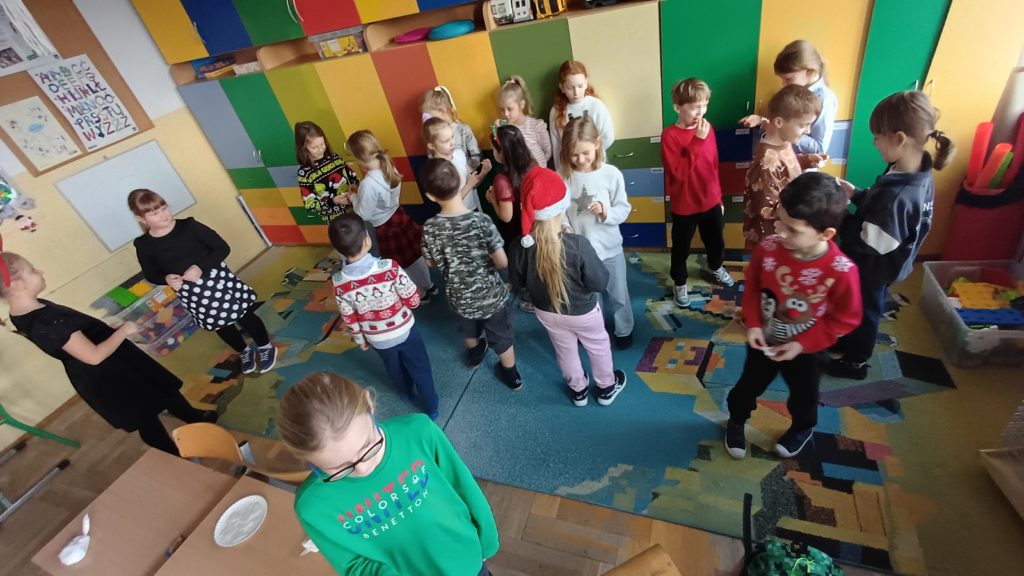 Grupa 20 uczniów z klasy 2d składa sobie życzenia i łamię się opłatkiem w klasie, stojąc na dywanie.