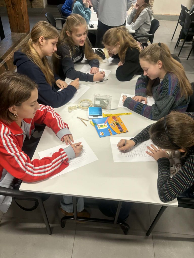 Grupa dziewczynek/ chłopców siedzi przy stole i wypełnia karty pracy