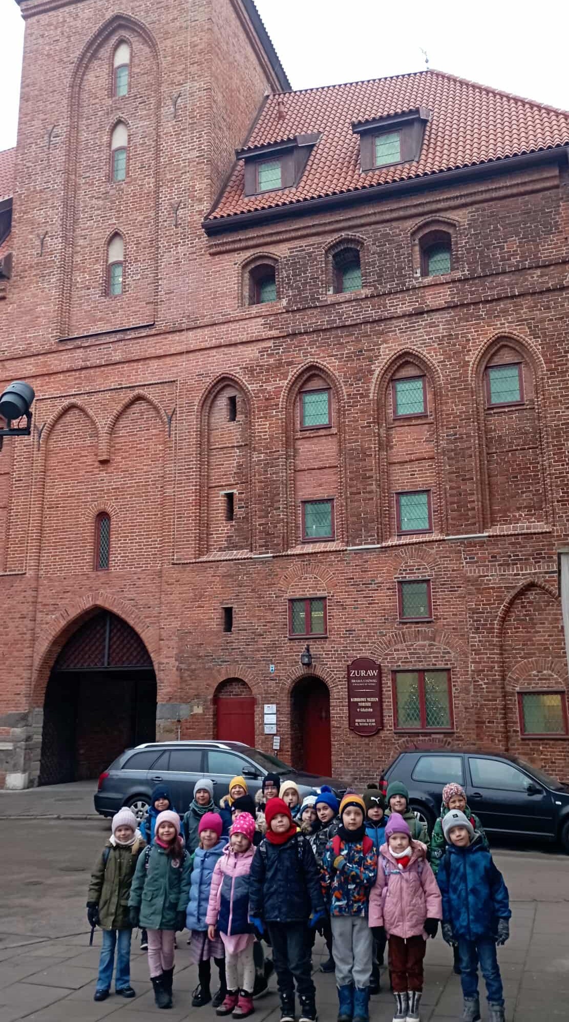 Na tle fasady budynku Żurawia przed wejściem do muzeum stoi grupa uczniów klasy 1c.