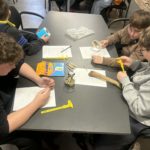 Grupa dziewczynek/ chłopców siedzi przy stole i wypełnia karty pracy