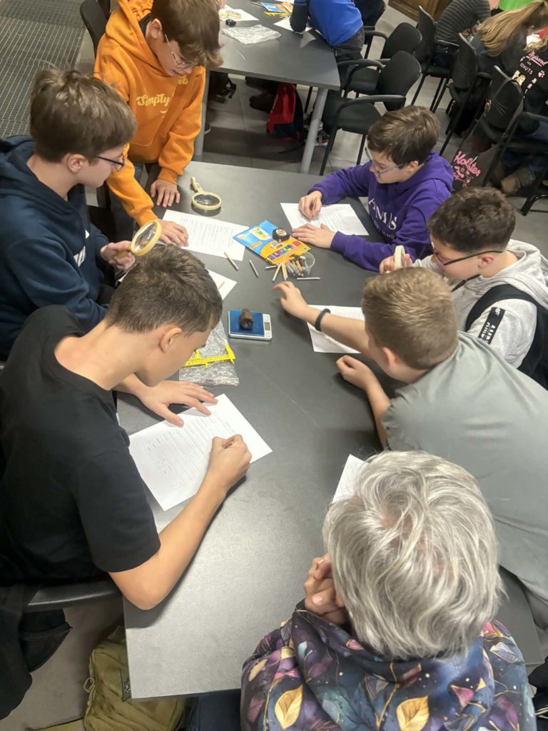 Grupa dziewczynek/ chłopców siedzi przy stole i wypełnia karty pracy