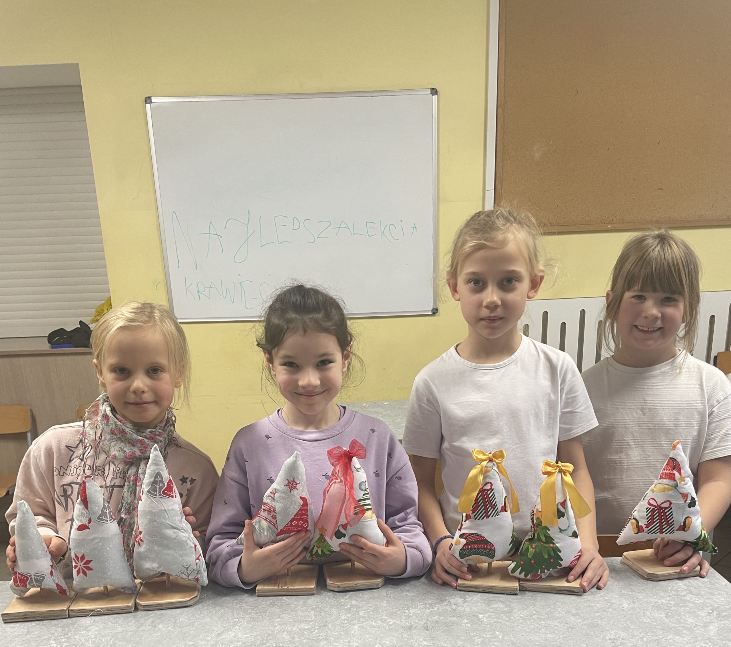 Cztery dziewczynki stoją za stołem na którym są uszyte choinki.