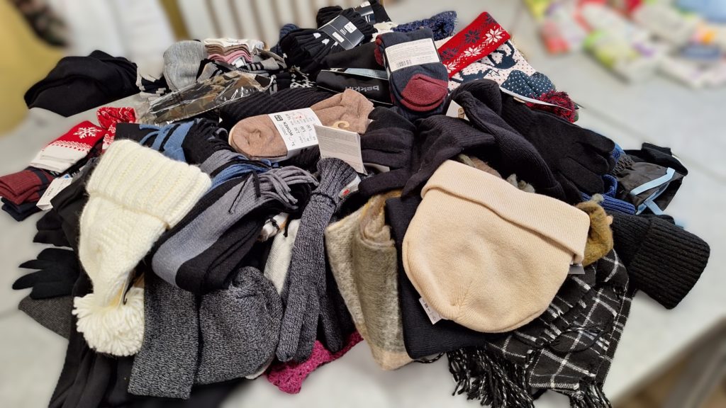 Na zdjęciu jest duża sterta zebranych zimowych ubrań: czapek, szalików, rękawiczek i skarpet ułożonych na stole.
