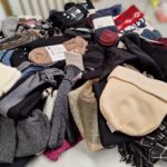 Na zdjęciu jest duża sterta zebranych zimowych ubrań: czapek, szalików, rękawiczek i skarpet ułożonych na stole.
